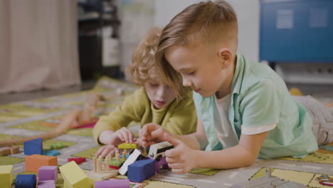 Zwei-Kleine-Jungs-Spielen-Mit-Holzstücken-Und-Auto-Liegen-Auf-Einem-Teppich-In-Einer-Montessori-Schulklasse