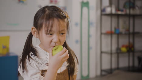 Little-Girl-Eating-An-Apple-In-Classroom-In-A-Montessori-School