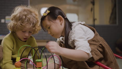Little-Girl-And-Little-Boy-Playing-With-Wooden-Pieces-That-Move-In-A-Wire-In-Classroom-In-A-Montessori-School