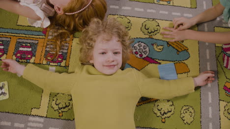 Top-View-Of-A-Little-Boy-Lying-On-The-Carpet-With-Open-Arms-And-Looking-At-Camera-1