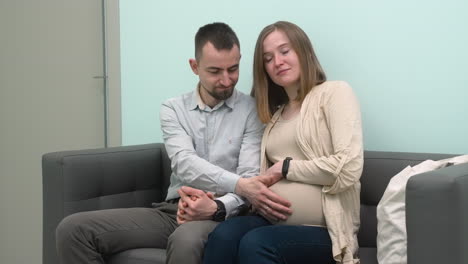 Loving-Pregnant-Couple-Sitting-In-Waiting-Room-For-A-Gynecological-Consultation
