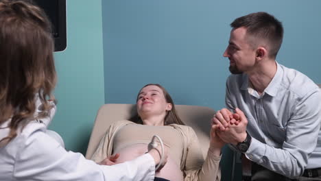 Schwangere-Frau-Mit-Ultraschalluntersuchung-Im-Gynäkologenbüro,-Während-Ihr-Liebevoller-Ehemann-Ihre-Hand-Hält-1