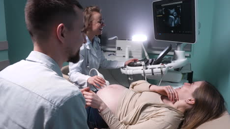 Female-Gynecologist-Showing-Image-Of-Fetus-On-Screen-Of-Ultrasound-Machine-To-Happy-Future-Parents