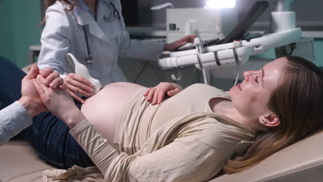 Schwangere-Frau-Mit-Ultraschalluntersuchung-Im-Gynäkologenbüro,-Während-Ihr-Liebevoller-Ehemann-Ihre-Hand-Hält-11