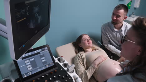 Pregnant-Woman-Having-Ultrasound-Scan-At-The-Gynecologist-Office-While-Loving-Husband-Holding-Her-Hand-12