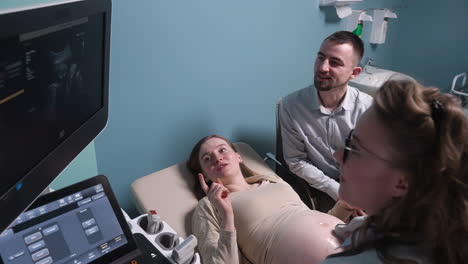 Female-Gynecologist-Showing-Image-Of-Fetus-On-Screen-Of-Ultrasound-Machine-To-Happy-Future-Parents-1