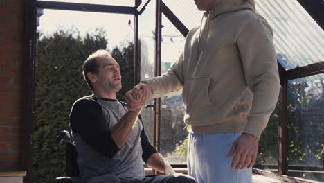 Disabled-Man-In-Wheelchair-And-His-Friend-Greeting-With-Handshake-And-Having-Fun-At-Home
