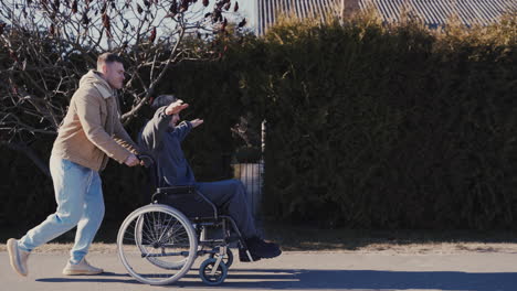 Junger-Mann-Läuft,-Während-Er-Seinen-Behinderten-Freund-Im-Rollstuhl-Schiebt-Und-Gemeinsam-Spaß-Hat