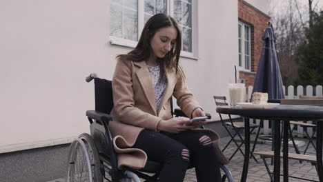 Happy-Disabled-Girl-In-Wheelchair-Using-Mobile-Phone-In-A-Bar-Terrace-1