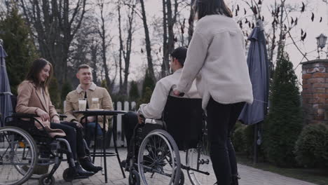 Junge-Frau-Und-Ihr-Behinderter-Freund-Im-Rollstuhl-Treffen-Sich-Mit-Anderen-Freunden-Auf-Einer-Barterrasse