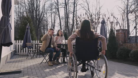 Rear-View-Of-Disable-Woman-In-Wheelchair-Meeting-Other-Friends-In-A-Bar-Terrace