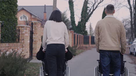 Rückansicht-Von-Frau-Und-Mann,-Die-Mit-Ihren-Behinderten-Freunden-Im-Rollstuhl-Durch-Die-Stadt-Spazieren-Gehen