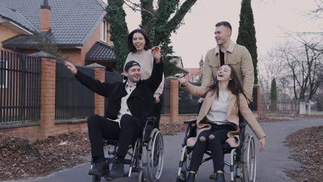 Frau-Und-Mann,-Die-Mit-Ihren-Behinderten-Freunden-Im-Rollstuhl-Laufen-Und-Zusammen-Spaß-Haben