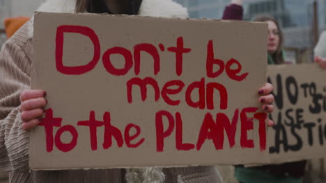Nahaufnahme-Eines-Pappplakats-Mit-Der-Phase-Sei-Nicht-Gemein,-Der-Planet,-Der-Von-Einer-Frau-Während-Eines-Protestes-Gegen-Den-Klimawandel-Gehalten-Wird