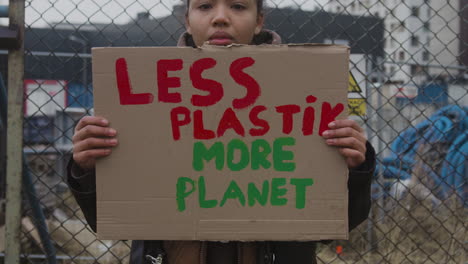 Close-Up-View-Of-Young-American-Female-Activist-Holding-A-Cardboard-Placard-Against-The-Use-Of-Plastics-During-A-Climate-Change-Protest-While-Looking-At-Camera-1