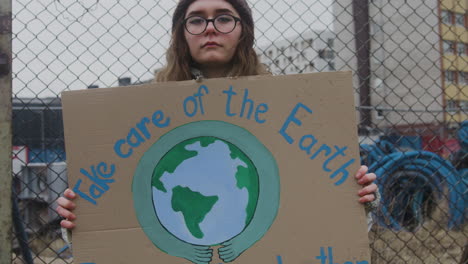 Junge-Aktivistin,-Die-Während-Eines-Protestes-Gegen-Den-Klimawandel-Ein-Plakat-Aus-Pappe-Hält,-Während-Sie-In-Die-Kamera-1-Blickt