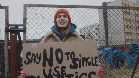 Young-Female-Activist-Holding-A-Cardboard-Placard-And-Protesting-To-Save-The-Earth-During-A-Climate-Change-Protest-While-Looking-At-Camera