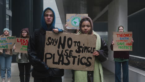 Jóvenes-Activistas-Masculinas-Y-Estadounidenses-Sosteniendo-Una-Pancarta-De-Cartón-Durante-Una-Protesta-Por-El-Cambio-Climático-Mientras-Miran-La-Cámara