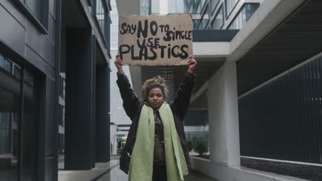 Young-American-Female-Activist-Holding-A-Cardboard-Placard-Against-The-Use-Of-Plastics-During-A-Climate-Change-Protest-While-Looking-At-Camera-1