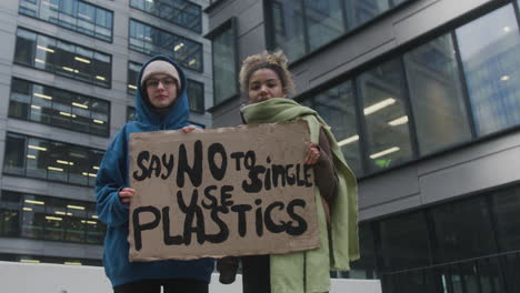 Dos-Jóvenes-Activistas-Climáticas-Sosteniendo-Una-Pancarta-Y-Protestando-Contra-Los-Plásticos-De-Un-Solo-Uso-Mientras-Miran-La-Cámara-2