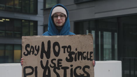 Junge-Klimaaktivistin-Mit-Transparent,-Die-Gegen-Einwegkunststoffe-Protestiert,-Während-Sie-In-Kamera-1-Blickt
