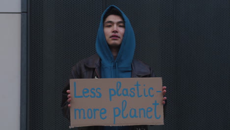 Junger-Aktivist,-Der-Während-Eines-Protestes-Gegen-Den-Klimawandel-Ein-Plakat-Aus-Pappe-Gegen-Die-Verwendung-Von-Plastik-Hält,-Während-Er-In-Die-Kamera-Schaut