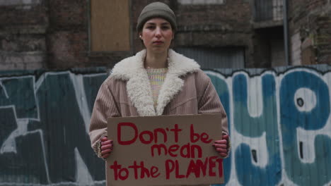 Young-Girl-Looking-At-Camera-And-Holding-A-Cardboard-Placard-With-The-Phase-Dont-Be-Mean-The-Planet-During-A-Climate-Change-Protest