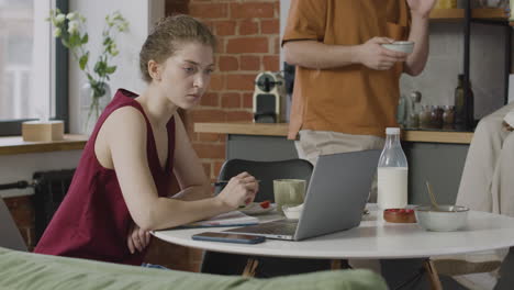 Girl-Having-Breakfast-And-Working-On-Laptop-Computer-In-A-Shared-Flat