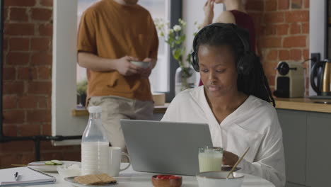 Girl-With-Headphones-Having-Breakfast-And-Working-On-Laptop-Computer-In-A-Shared-Flat-1