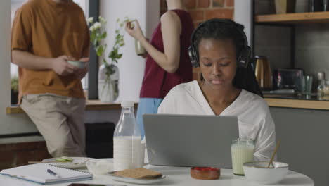 Girl-With-Headphones-Having-Breakfast-And-Working-On-Laptop-Computer-In-A-Shared-Flat-2