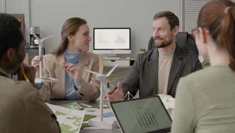 Woman-Explaining-Wind-Turbine-Model-And-Discussing-About-Renewable-Energy-Project-With-Her-Colleagues-In-The-Office