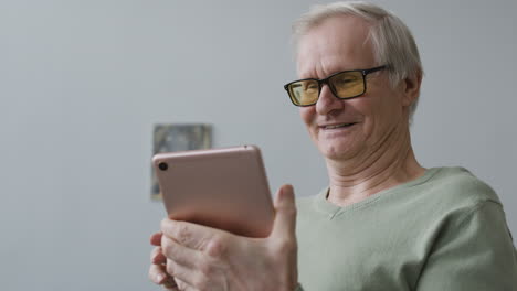 Happy-Senior-Man-Using-Tablet-While-Standing-In-The-Living-Room-Of-A-Modern-Apartment