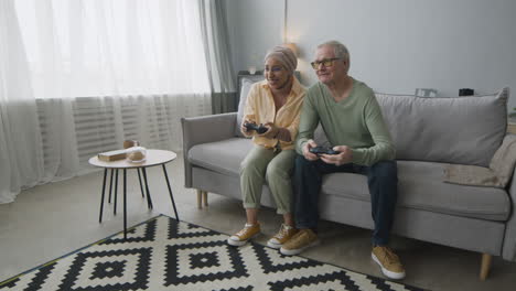Happy-Middle-Aged-Arabic-Woman-And-Senior-Man-Playing-Video-Game-While-Sitting-On-Sofa-At-Home