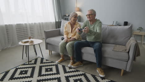 Glückliche-Arabische-Frau-Mittleren-Alters-Und-älterer-Mann-Spielen-Videospiel,-Während-Sie-Zu-Hause-Auf-Dem-Sofa-Sitzen-1