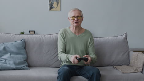 Happy-Senior-Man-Playing-Video-Game-While-Sitting-On-Sofa-At-Home