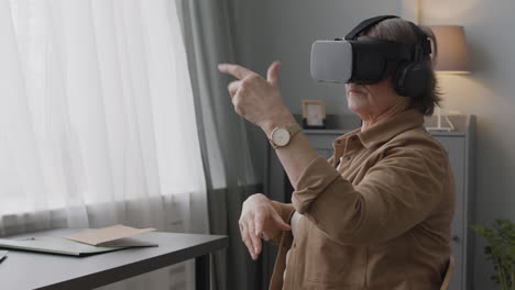 Senior-Woman-Using-Virtual-Reality-Headset-Glasses-And-Moving-Her-Hands-While-Sitting-On-Chair-In-A-Modern-Living-Room-2