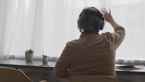 Seniorin,-Die-Eine-Virtual-Reality-Headset-Brille-Verwendet-Und-Ihre-Hände-Bewegt,-Während-Sie-Auf-Einem-Stuhl-In-Einem-Modernen-Wohnzimmer-Sitzt-3