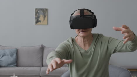 Senior-Man-Using-Virtual-Reality-Headset-Glasses-And-Moving-His-Hands-While-Sitting-On-Chair-In-A-Modern-Living-Room-1