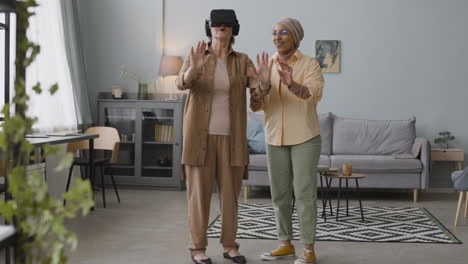 Arabische-Frau-Mittleren-Alters,-Die-Einer-älteren-Dame-Hilft,-Zu-Hause-Eine-Virtual-Reality-Headset-Brille-Zu-Verwenden-1