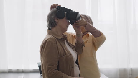 Middle-Aged-Arabic-Woman-Helping-A-Senior-Lady-To-Use-Virtual-Reality-Headset-Glasses-At-Home-3