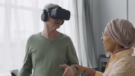 Middle-Aged-Arabic-Woman-Helping-A-Happy-Senior-Man-To-Use-Virtual-Reality-Headset-Glasses-At-Home
