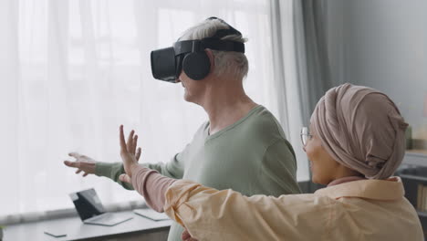 Middle-Aged-Arabic-Woman-Helping-A-Happy-Senior-Man-To-Use-Virtual-Reality-Headset-Glasses-At-Home-1