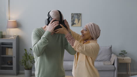 Mujer-árabe-De-Mediana-Edad-Ayudando-A-Un-Anciano-Feliz-A-Usar-Gafas-De-Realidad-Virtual-En-Casa-2