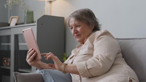Lächelnde-ältere-Frau,-Die-Ein-Tablet-Verwendet,-Während-Sie-Zu-Hause-Auf-Dem-Sofa-Liegt-1