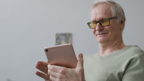Smiling-Senior-Man-Using-Tablet-While-Sitting-In-A-Modern-Living-Room-At-Home
