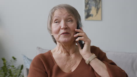 Anciana-Llamando-Por-Teléfono-Inteligente-Sentada-En-Casa