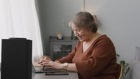 Senior-Woman-Sitting-At-Desk-At-Home-While-Using-Laptop