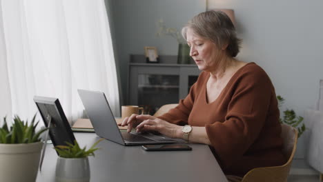 Focused-Woman-Typewritting-At-Laptop-Sitting-At-Desk-At-Home-1