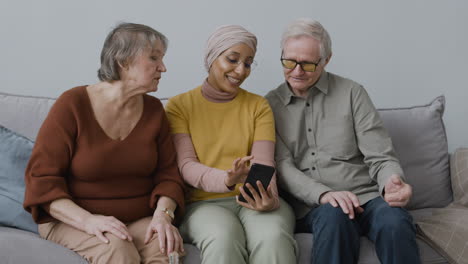Vorderansicht-Einer-Arabischen-Frau,-Die-Einer-älteren-Frau-Und-Einem-älteren-Mann-Beibringt,-Ein-Smartphone-Zu-Benutzen