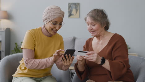 Arabic-Woman-Teaching-An-Elderly-Woman-To-Use-Mobile-Payment-With-Credit-Card
